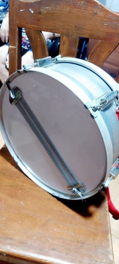 Fissler By Global Snare Drum (Category: Musical Instruments) located in Quezon City. Submitted by tinypeep.ph (Listing ID 1449678786, Image 3). Description: - Fissler snare drum by Global - Features a red strap - Drum head shows some bubbling and wear - Snare wires are attached and functional - Ideal for practice sessions or beginner drummers.