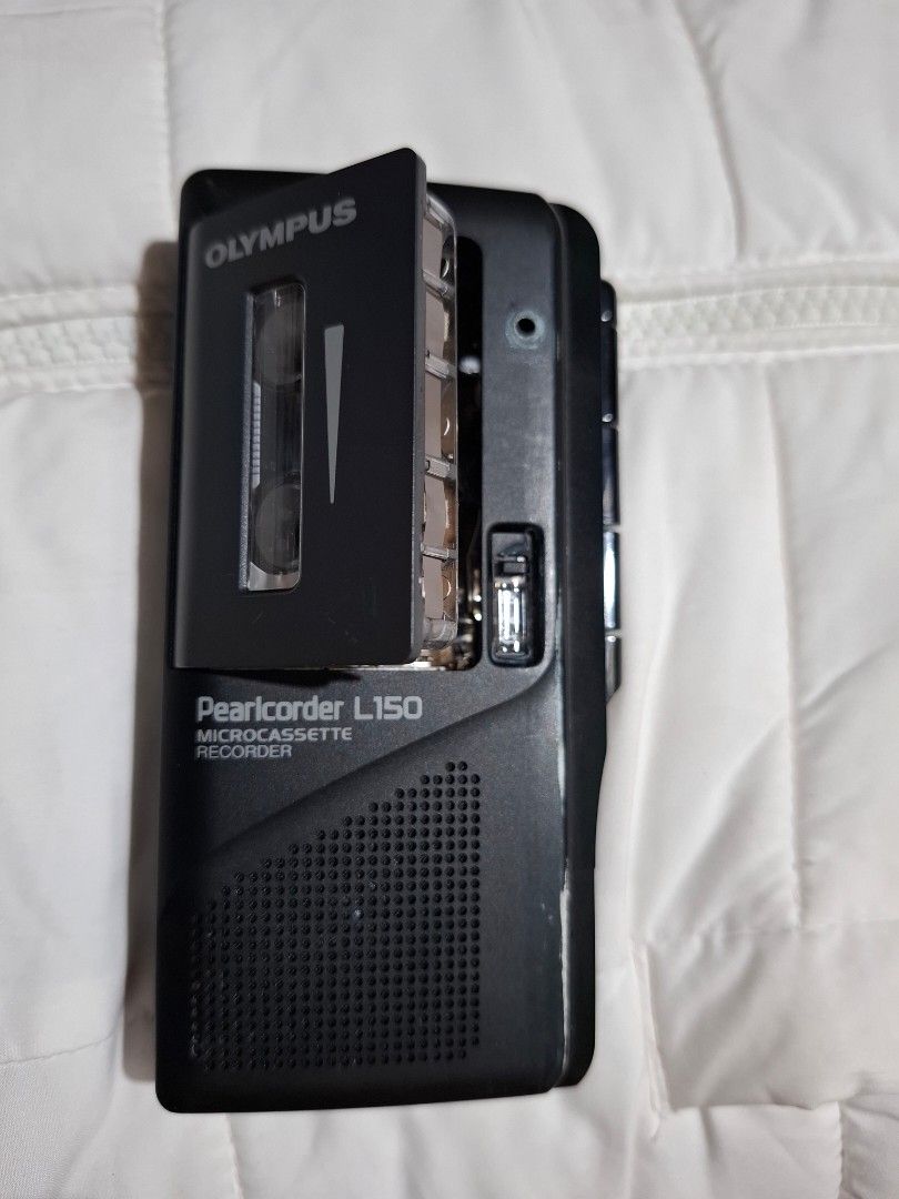 OLYMPUS PEARLCORDER L150 (Category: Portable Audio Accessories) located in Carcar. Submitted by brave_brandboss (Listing ID 1449720299, Image 1). Description: The selected region shows an Olympus Pearlcorder L150 microcassette tape recorder. This vintage voice recorder uses compact microcassettes and was a popular portable device for interviews, dictation, and lectures during its era. Key features of this model include: Dual Tape Speeds: Allows y