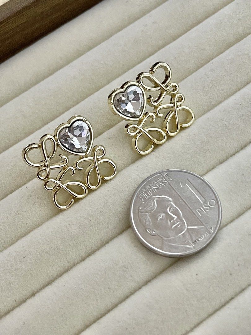 Loewe Inspired Heart Crystal Stud Earrings (Category: Earrings) located in Pasig City. Submitted by Jo.JewelsofVVM (Listing ID 1450134577, Image 3). Description: - Gold tone stud earrings - Features a heart-shaped crystal - Stylized 'LOEWE' lettering - Easy to wear stud design - Adds sparkle to any outfit - Perfect for gifting or personal treat.