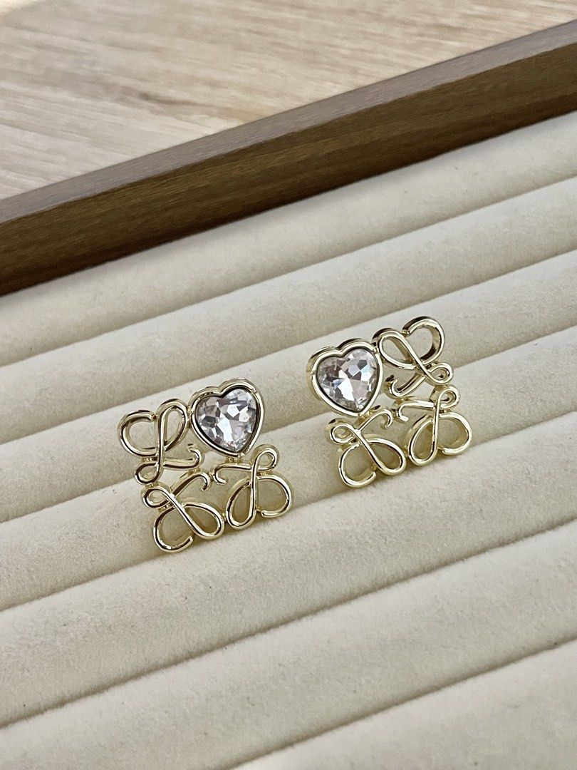 Loewe Inspired Heart Crystal Stud Earrings (Category: Earrings) located in Pasig City. Submitted by Jo.JewelsofVVM (Listing ID 1450134577, Image 2). Description: - Gold tone stud earrings - Features a heart-shaped crystal - Stylized 'LOEWE' lettering - Easy to wear stud design - Adds sparkle to any outfit - Perfect for gifting or personal treat.