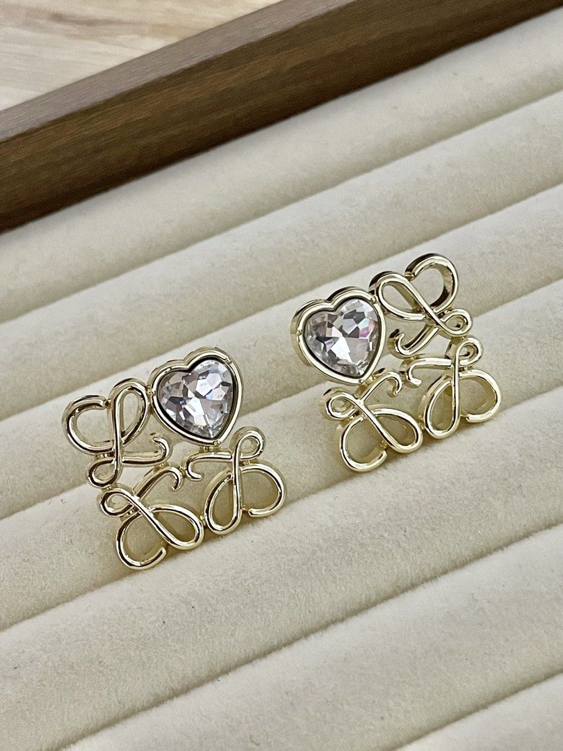 Loewe Inspired Heart Crystal Stud Earrings (Category: Earrings) located in Pasig City. Submitted by Jo.JewelsofVVM (Listing ID 1450134577, Image 1). Description: - Gold tone stud earrings - Features a heart-shaped crystal - Stylized 'LOEWE' lettering - Easy to wear stud design - Adds sparkle to any outfit - Perfect for gifting or personal treat.