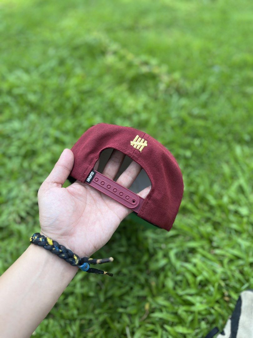 Undefeated Burgundy Corduroy Snapback Hat (Category: Caps & Hats) located in Bulacan. Submitted by sef19 (Listing ID 1449961724, Image 1). Description: - Burgundy corduroy snapback from Undefeated - Gold embroidered 'Undefeated' script on the front - Small gold '5 strikes' logo on the back - Adjustable snap closure for a custom fit - Crafted from a comfortable acrylic and wool blend.