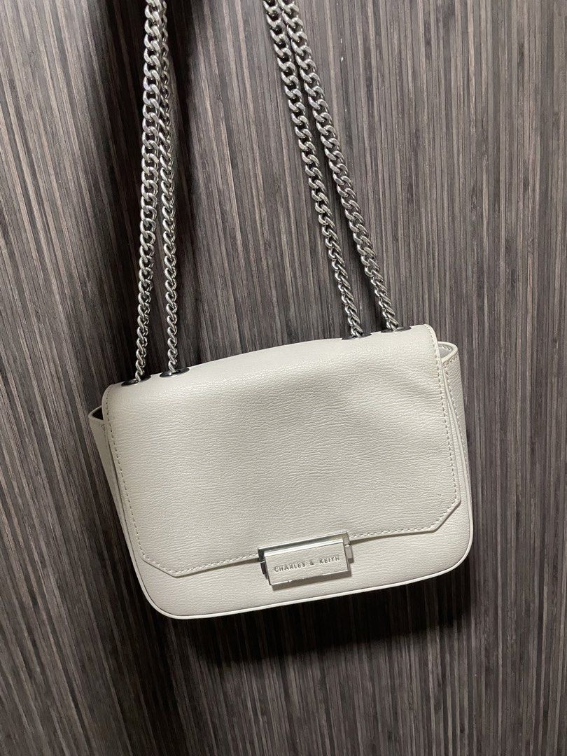 Charles & Keith White Leather Chain Crossbody Bag (Category: Cross-body Bags) located in Caloocan City. Submitted by chraefm (Listing ID 1450162980, Image 1). Description: - White leather crossbody bag by Charles & Keith - Features a chic silver chain strap - Secure flap closure with a metal clasp - Convenient back pocket for easy access - Shows minor signs of wear on the back pocket area - Ideal for casual outings and everyday style with dust ba