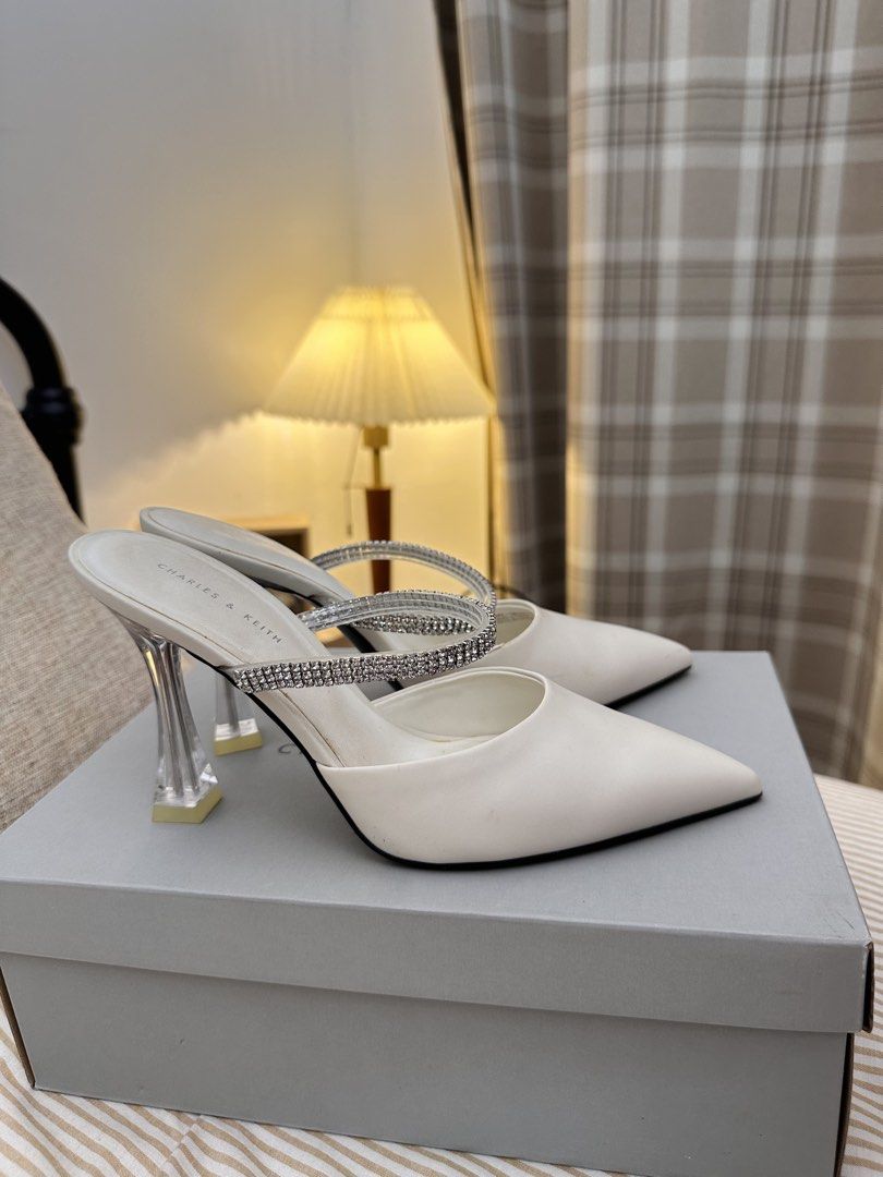 Charles & Keith White Mules with Rhinestone Strap and Clear Heel (Category: Heels) located in Kuala Lumpur. Submitted by ntsharusli (Listing ID 1450424139, Image 3). Description: - Brand: Charles & Keith - Style: White pointed-toe mules - Size: 38 - Features: Sparkly rhinestone strap, clear sculpted heel - Closure: Slip-on - Condition: Comes with original box.