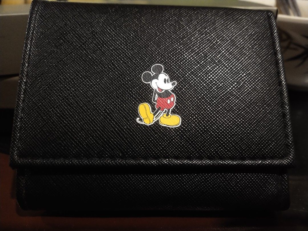Black Tri-fold Wallet with Mickey Mouse Emblem (Category: Wallets & Card holders) located in Tuba. Submitted by drickbernard (Listing ID 1450528429, Image 1). Description: - Cute black tri-fold wallet - Classic Mickey Mouse emblem on the front - Multiple card slots inside - Coin compartment with snap closure - Small and compact for easy carrying - Ideal for Disney enthusiasts.