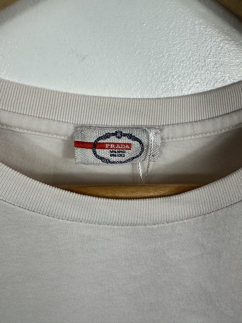 Prada White Pocket T-Shirt XL (Category: Tshirts & Polo Shirts ) located in Manila. Submitted by collect__ph (Listing ID 1447131987, Image 2). Description: - Authentic Prada Pocket Tee - Size: 26.5” L x 22” W - Signature red Prada tab on the side - Material: 100% Cotton - Care: Wash cold, inside out, separately. Do not soak/wring. Iron on dry clean setting..