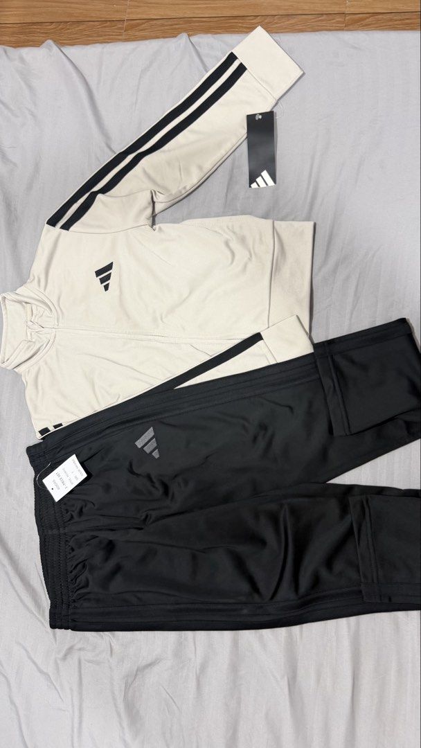 Adidas Tracksuit Set - Beige Jacket & Black Pants (Category: Babies & Kids Fashion) located in Manila. Submitted by eah0416 (Listing ID 1450756552, Image 1). Description: - Classic Adidas tracksuit set - Light beige jacket with iconic black three stripes on sleeves - Black pants with matching black three stripes - Features Adidas logos on both jacket and pants - Versatile for athletic activities or everyday casual style.