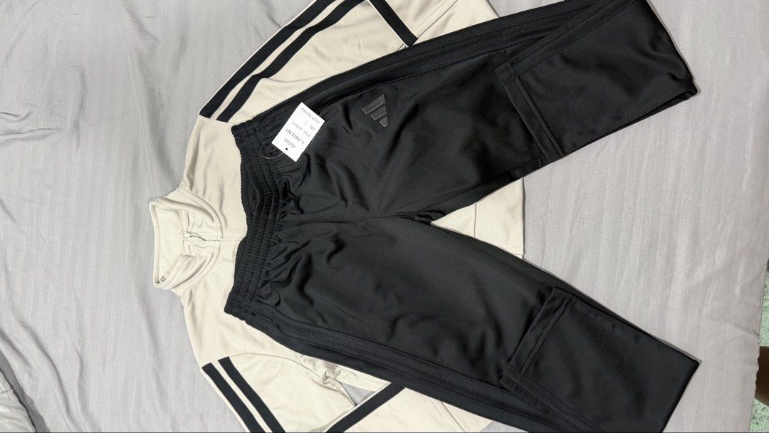 Adidas Tracksuit Set - Beige Jacket & Black Pants (Category: Babies & Kids Fashion) located in Manila. Submitted by eah0416 (Listing ID 1450756552, Image 3). Description: - Classic Adidas tracksuit set - Light beige jacket with iconic black three stripes on sleeves - Black pants with matching black three stripes - Features Adidas logos on both jacket and pants - Versatile for athletic activities or everyday casual style.