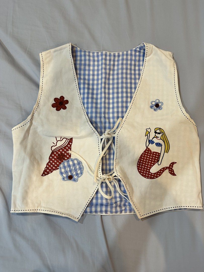 Cider Gingham Reversible Vest (Category: Sleeveless) located in Paranaque City. Submitted by applemt (Listing ID 1450868947, Image 3). Description: - One side: Blue gingham - Other side: White with mermaid, shell, and flower appliques - Ties at the front - Size Large, tag removed as it’s scratching my back - Armpit to armpit laid flat: 19”.