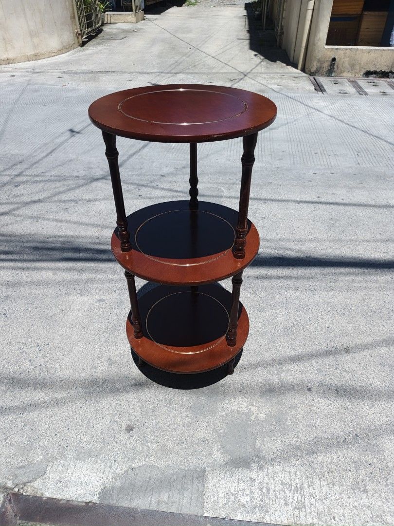 3-Tier Round Wooden Side Table (Category: Tables & Sets) located in Valenzuela. Submitted by kendra071914 (Listing ID 1450943385, Image 2). Description: - Three-tier round side table - Dark wood finish with lighter wood edge accents - Middle and bottom shelves are black - Stands approximately 76cm tall - Diameter of 38cm - Ideal for displaying plants or decorative items.