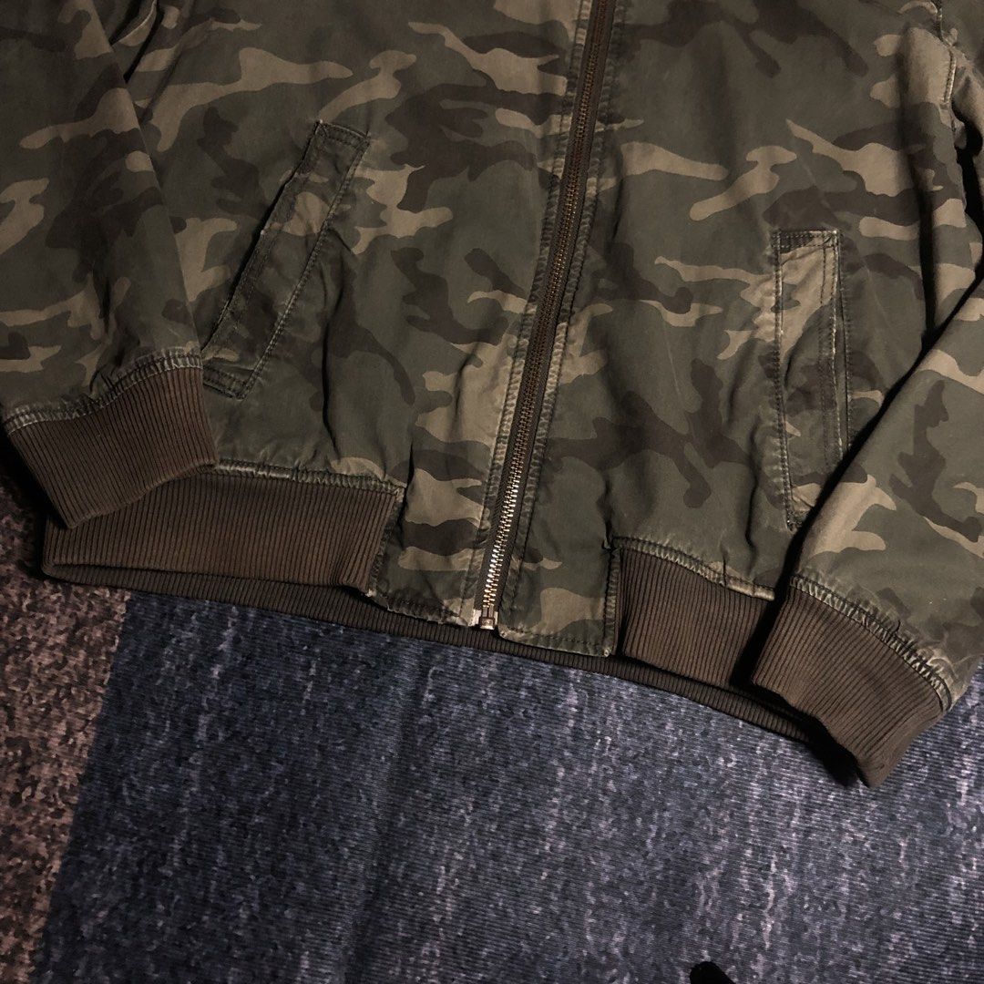 Camo Bomber Jacket with Grey Hood (Category: Coats, Jackets and Outerwear) located in Dasmarinas. Submitted by johnlloydm99208 (Listing ID 1451058633, Image 3). Description: - Green camouflage bomber jacket - Features a grey contrast hood - Ribbed cuffs and hem for a snug fit - Zipper closure for easy wear - Two convenient front pockets - Ideal for casual outfits, pairs well with jeans or joggers - 23x26.