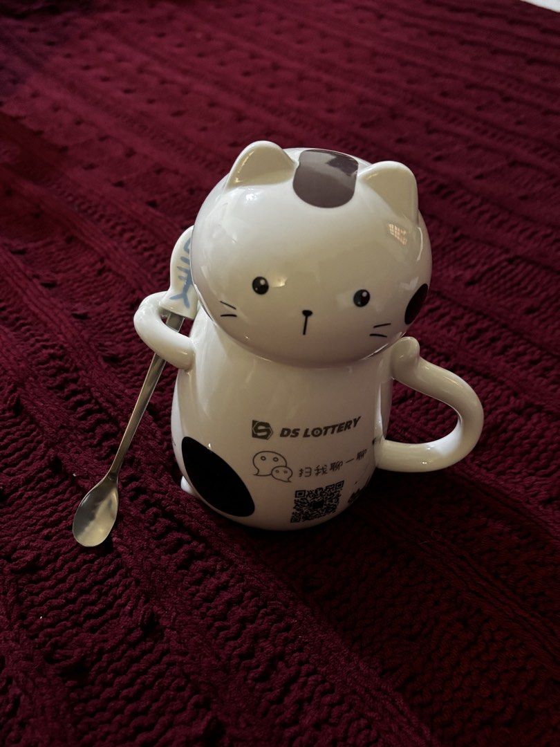 Cute Cat Ceramic Mug with Spoon (Category: Coffee & Tea Tableware) located in Manila. Submitted by mavria (Listing ID 1450981775, Image 1). Description: - White cat mug with black cat details. - Includes a matching spoon. - Features 'DS LOTTERY' branding and a QR code. - Unsealed and Unused note: > SF NOT INCLUDED > MOP: GCASH.