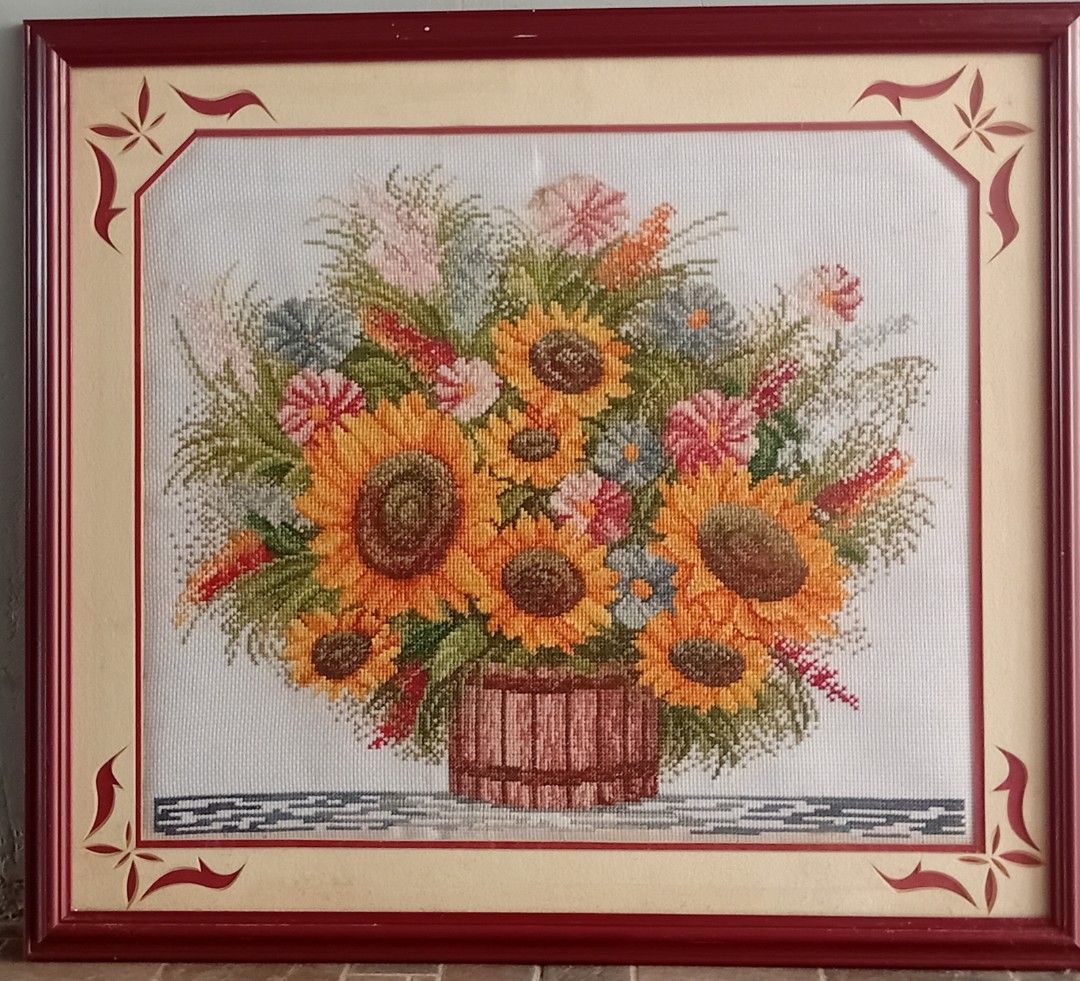 Framed Sunflower Cross-Stitch Artwork (Category: Art & Prints) located in Marikina City. Submitted by nico.outlet (Listing ID 1451109533, Image 1). Description: - Stunning framed cross-stitch featuring vibrant sunflowers in a wooden bucket. - Intricate details in the flowers and lush greenery. - Elegant deep red frame with cream matting and decorative corner accents. - Adds a bright and cheerful touch to any room. - Comes ready to hang. - Dimensi