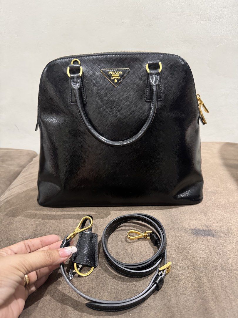 Prada Saffiano Leather Black Dome Handbag (Category: Luxury Bags & Wallets) located in Quezon City. Submitted by derill_shop (Listing ID 1451022954, Image 1). Description: - Classic black Prada dome handbag - Made from durable Saffiano leather - Elegant gold hardware details - Includes a detachable shoulder strap for versatile carrying - Comes with a signature Prada key charm - Spacious interior to hold your essentials - Ideal for both work and e