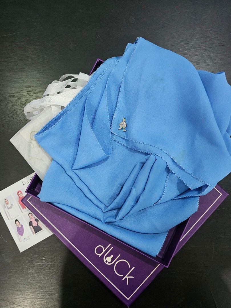The Duck Scarves Blue Shawl with Box (Category: Hijabs) located in Gelang Patah. Submitted by prelovedwardrobeclothing (Listing ID 1451005959, Image 1). Description: - Blue shawl from The Duck Scarves - Includes original box - Small stain present on fabric (refer to close-up photo) - Comes with white tissue paper, charm, ribbon - Ideal for everyday wear price including postage.