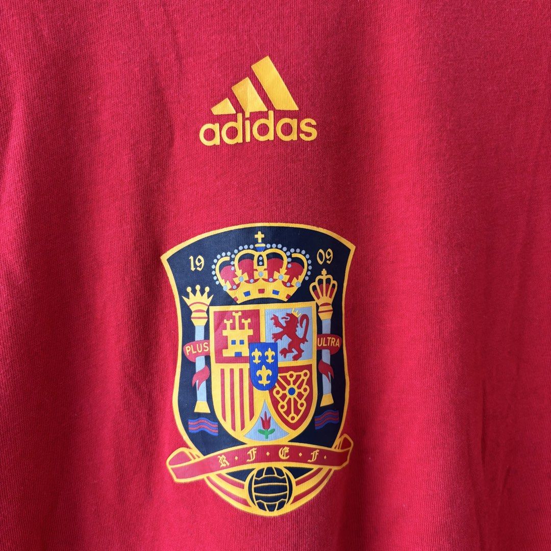 Adidas tee (Category: Formal Shirts) located in San Fernando. Submitted by diff.thr1ft (Listing ID 1451147126, Image 2). Description: - Brand: Adidas - Color: Red - Design: Features Spain national team crest and Adidas stripes - Material: 100% Cotton - Size: XL (UK 44 / US 44 / EU 54) - Condition: Layered condition 4 (good) - Perfect for football fans and casual wear.