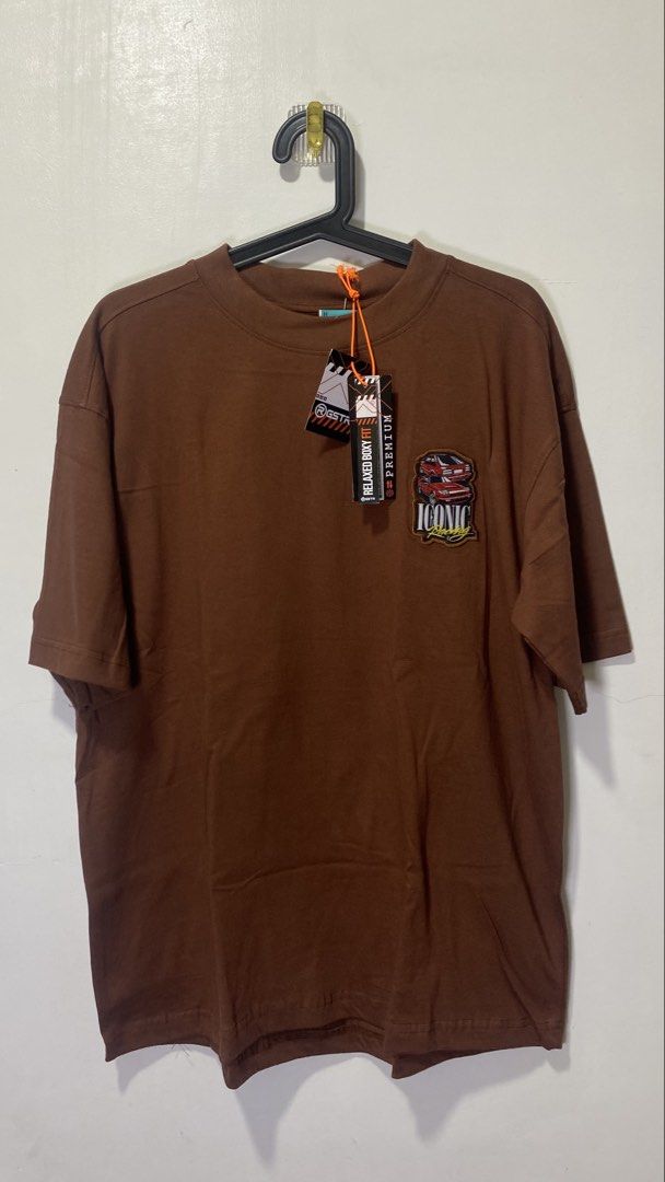 Brown Iconic Racing Graphic T-shirt (Category: Tshirts & Polo Shirts ) located in Taguig. Submitted by markaisie (Listing ID 1451146455, Image 2). Description: - Stylish brown t-shirt - Features a cool graphic on the back - Graphic includes two red cars and 'Iconic Racing' text - Also has 'Top Speed' and a checkered flag detail - Comfortable, oversized fit - Ideal for casual wear.