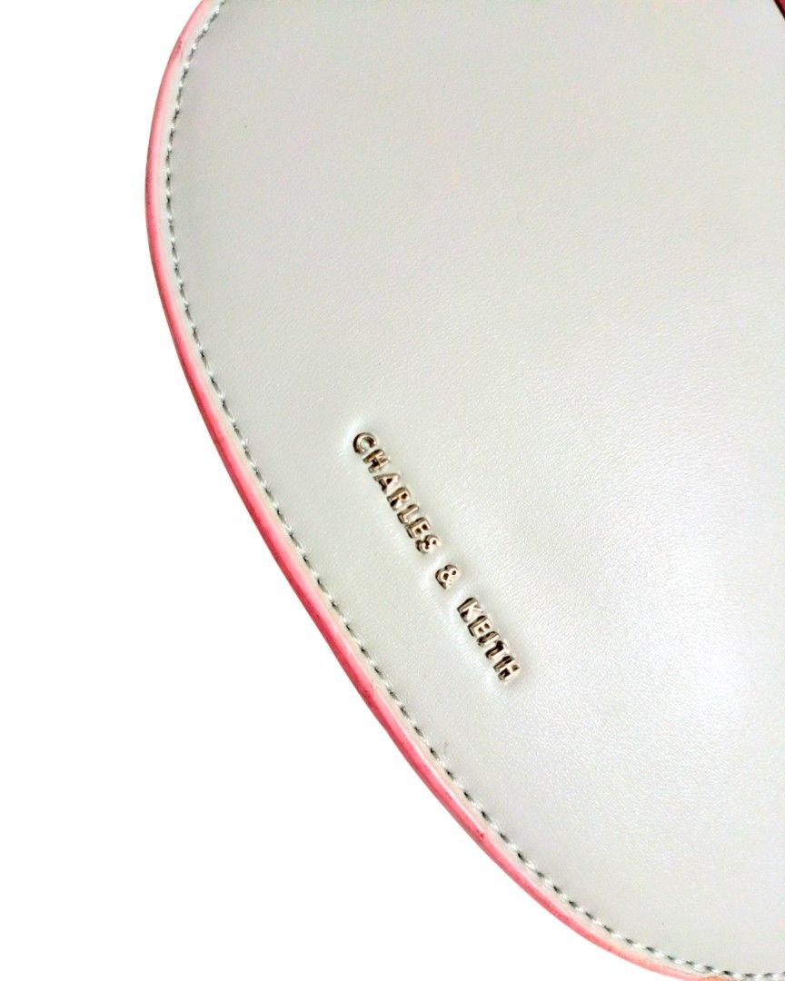 Charles & Keith Grey & Pink Top Handle Bag (Category: Shoulder Bags) located in Pasig City. Submitted by chaiselects (Listing ID 1451293307, Image 2). Description: - Cute half-moon shaped bag - Brand: Charles & Keith - Color: Light grey with pink trim and handle detail - Closure: Twist lock - Includes: Detachable strap - Versatile: Great for casual outings or dressing up an outfit.