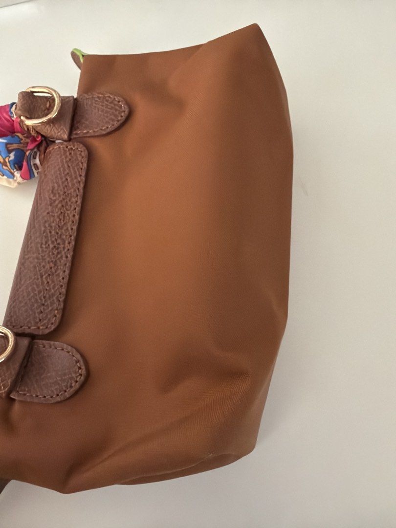 Longchamp Le Pliage pouch cognac (Category: Luxury Bags & Wallets) located in Makati City. Submitted by somethingownedbyme (Listing ID 1451201289, Image 3). Description: - Brown Longchamp handbag - Small size, ideal for essentials - Features leather trim and handles - Adorned with a colorful silk scarf tied around the handles - Snap button closure on the flap - Zipper closure for the main compartment - Clean inside and out - Ready for its new own