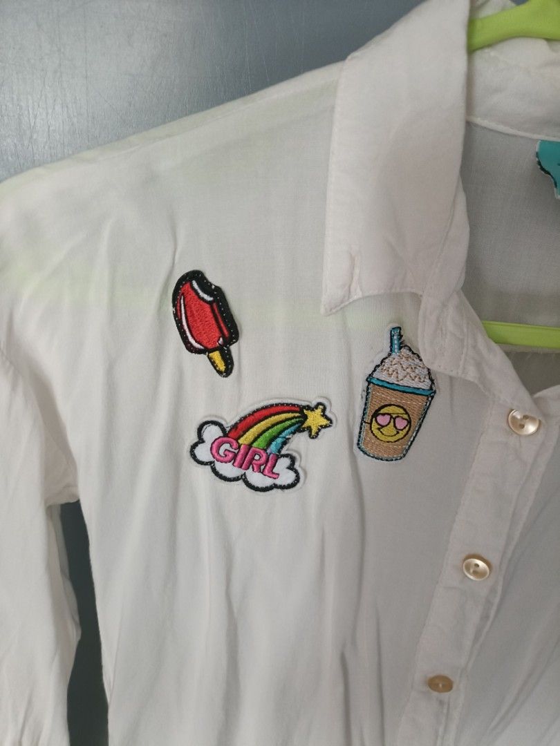 White Shirt with Patches - Size 10 (Category: Babies & Kids Fashion) located in Quezon City. Submitted by qcard13 (Listing ID 1451135799, Image 2). Description: - White long-sleeved shirt - Brand: Twilo - Size: 10, may fit 7-10 year old girls depending on their built. - Adorable embroidered patches: ice cream, rainbow with 'GIRL', coffee cup with sunglasses - Button-down front - Versatile for casual styling.