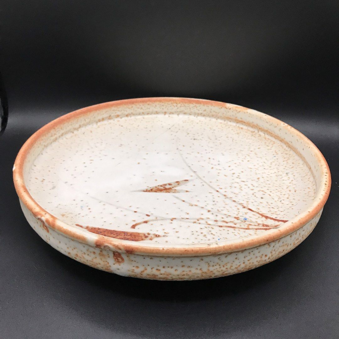 Footed Flat Textured Ceramic Bowl (Category: Dinnerware & Cutlery) located in Baao. Submitted by all.things.japan (Listing ID 1451513994, Image 2). Description: -9.75 x 1.8 inches Rustic ceramic plate with a speckled glaze. Features a hand-painted design with reddish-brown accents. Has three small feet on the underside. Great for serving or as a decorative piece. Unique, artisanal look. Measures approximately [insert diameter here] inches across.