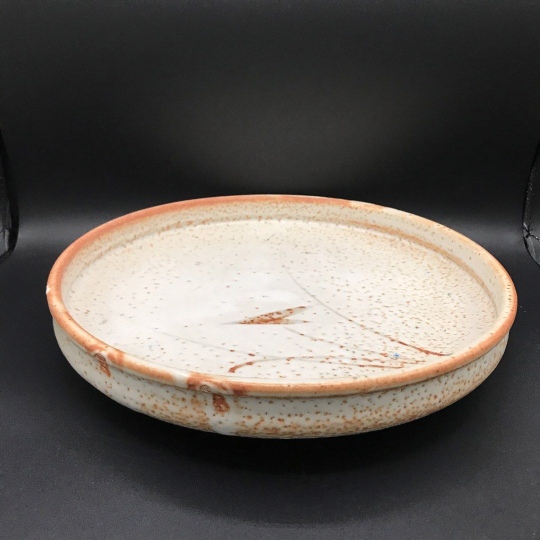 Footed Flat Textured Ceramic Bowl (Category: Dinnerware & Cutlery) located in Baao. Submitted by all.things.japan (Listing ID 1451513994, Image 3). Description: -9.75 x 1.8 inches Rustic ceramic plate with a speckled glaze. Features a hand-painted design with reddish-brown accents. Has three small feet on the underside. Great for serving or as a decorative piece. Unique, artisanal look. Measures approximately [insert diameter here] inches across.