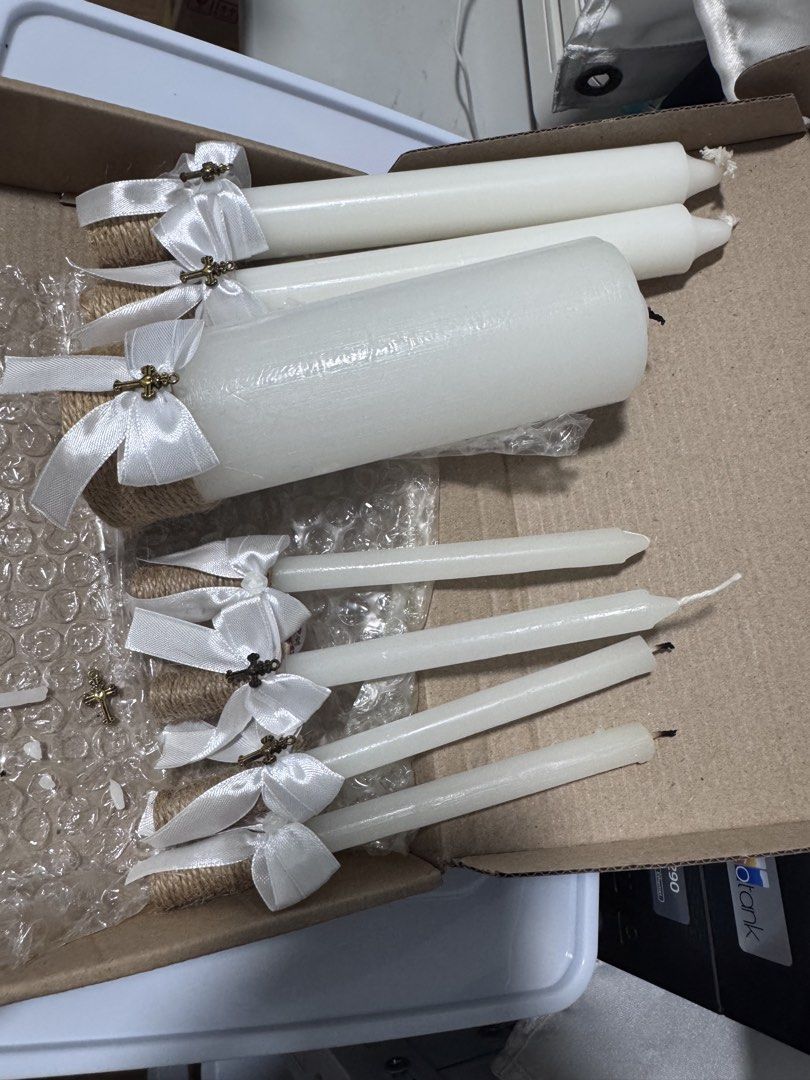 White Taper Candles with Cross Embellishments (Category: Home Fragrance) located in Manila. Submitted by abic7 (Listing ID 1451356787, Image 1). Description: - Set of 7 white taper candles - Each candle features twine at the base - Tied with a white satin ribbon - Adorned with a small gold-tone cross charm - Ideal for BAPTISMAL.