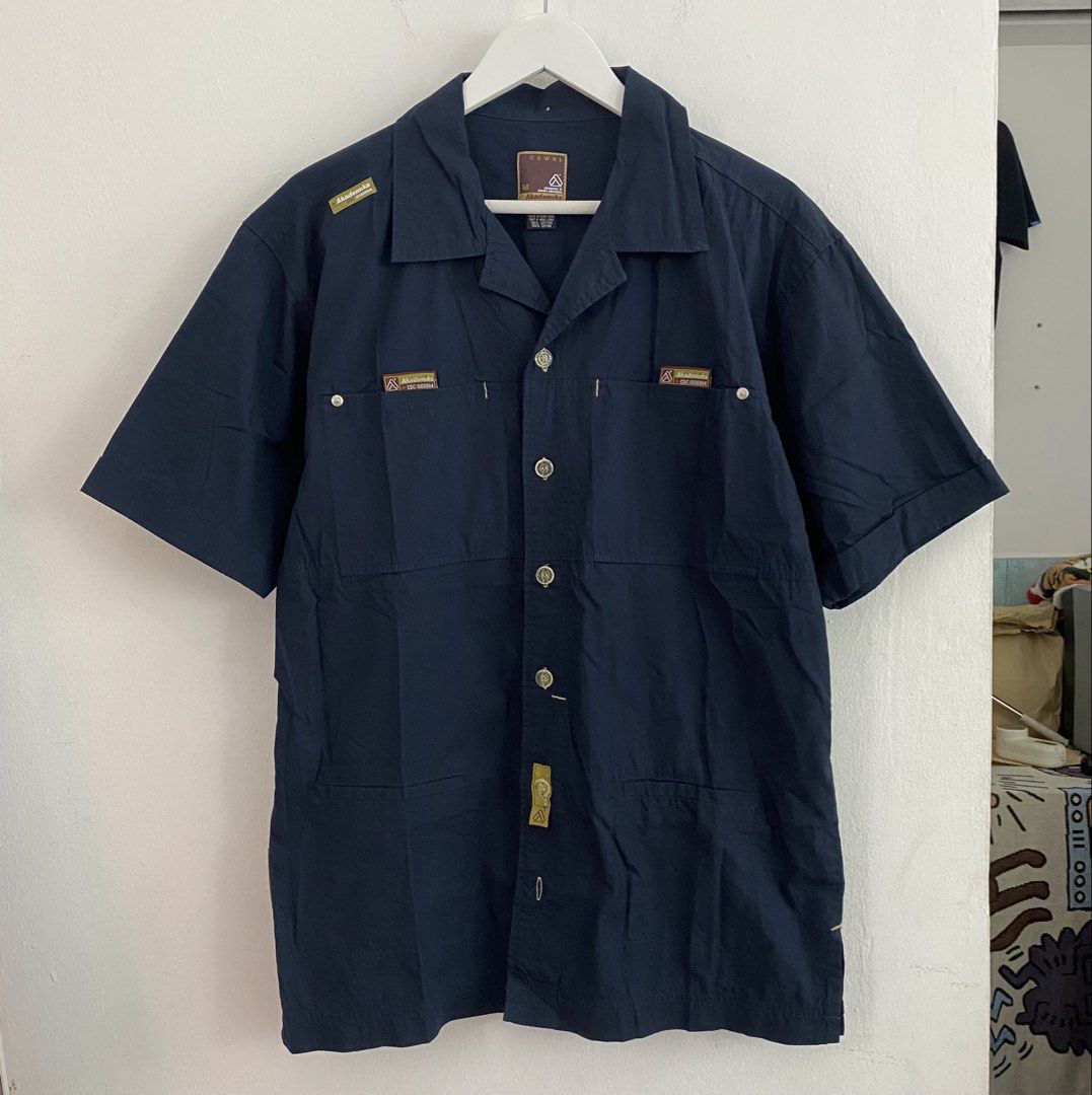 Akademiks Short Sleeve Button Up Shirt Size M (Category: Tshirts & Polo Shirts ) located in Cavite. Submitted by mana__ (Listing ID 1451691519, Image 2). Description: - Navy blue short sleeve button up shirt - Size Medium (M) - Unique graphic print on the back (two figures & '28') - Multiple front pockets with branded details - Ideal for casual wear.