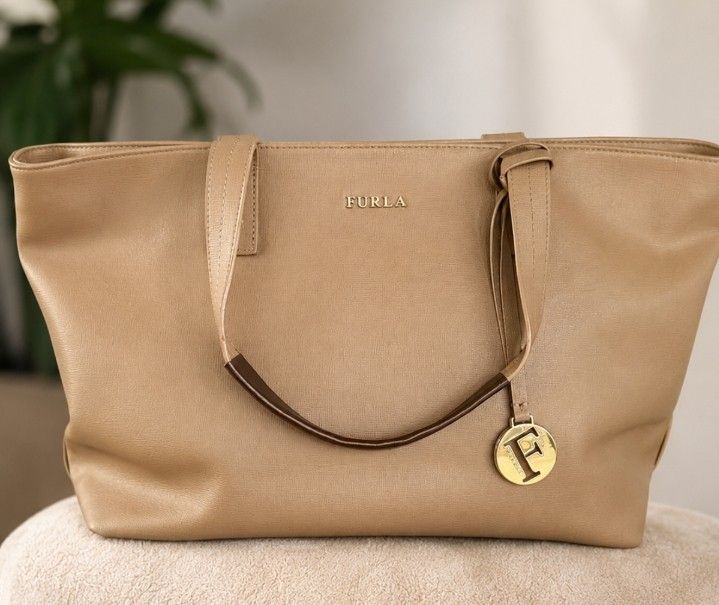 Furla Tote Bag Beige Leather (Category: Tote Bags) located in Kuala Kurau. Submitted by fiverose86 (Listing ID 1451646695, Image 1). Description: - Beige Furla tote bag - Spacious interior - Zippered top closure - Lined with Furla logo pattern - Fits a laptop - Ideal for everyday use or work.