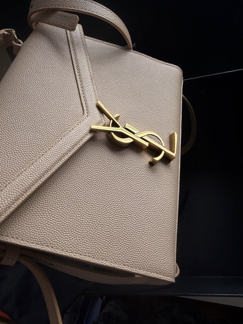 Y S L Beige Leather Handbag (Category: Luxury Bags & Wallets) located in Las Pinas. Submitted by twiceloved24 (Listing ID 1451586231, Image 2). Description: - Iconic gold logo prominently displayed on the front. - Versatile carrying options: top handle and adjustable shoulder strap. - Interior features embossed 'Saint Laurent Paris' detail. - Comes complete with original dust bag and box. - Ideal accessory for both daytime and evening wear..