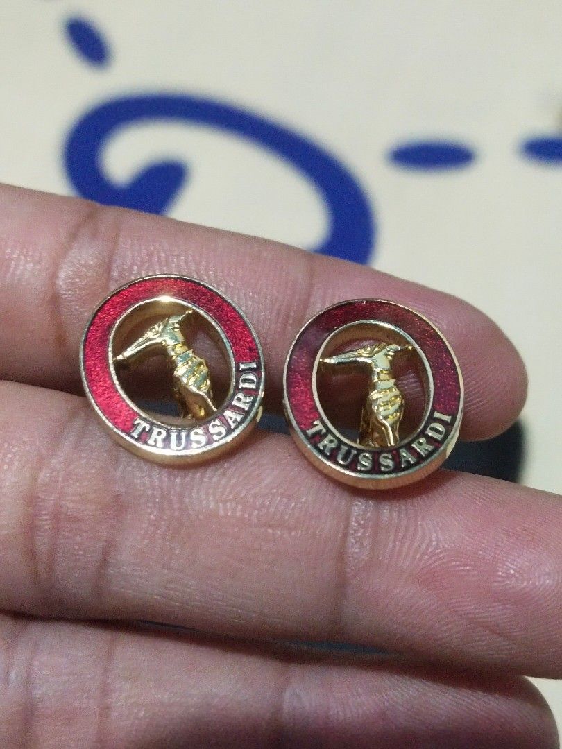 Trussardi Gold Red Enamel Cufflinks (Category: Cuff Links) located in Tuba. Submitted by drickbernard (Listing ID 1451692341, Image 2). Description: - Brand: Trussardi - Material: Gold tone with red enamel - Design: Features the iconic Trussardi greyhound logo - Occasion: Ideal for formal wear or adding flair to any shirt - Includes: One pair of cufflinks.