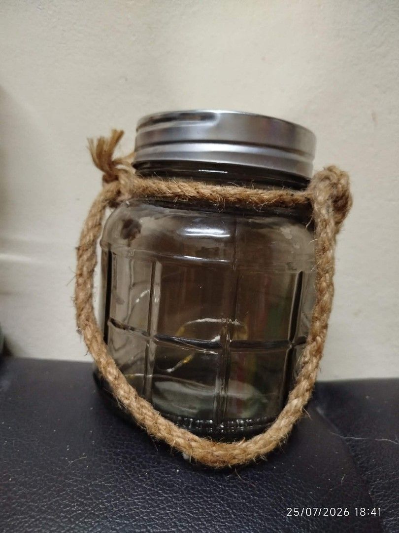 Decorative Glass Jar with Rope Handle (Category: Vases & Decorative Bowls) located in Quezon City. Submitted by chadrison (Listing ID 1451826476, Image 1). Description: - Charming rustic glass jar - Features a textured glass pattern - Comes with a sturdy rope handle - Includes a silver-colored metal lid - Ideal for storage or as a decorative accent - Approximately 10cm in height.