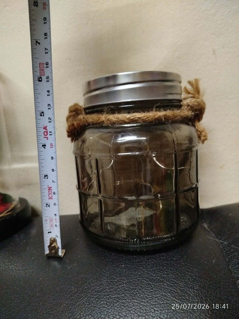 Decorative Glass Jar with Rope Handle (Category: Vases & Decorative Bowls) located in Quezon City. Submitted by chadrison (Listing ID 1451826476, Image 3). Description: - Charming rustic glass jar - Features a textured glass pattern - Comes with a sturdy rope handle - Includes a silver-colored metal lid - Ideal for storage or as a decorative accent - Approximately 10cm in height.