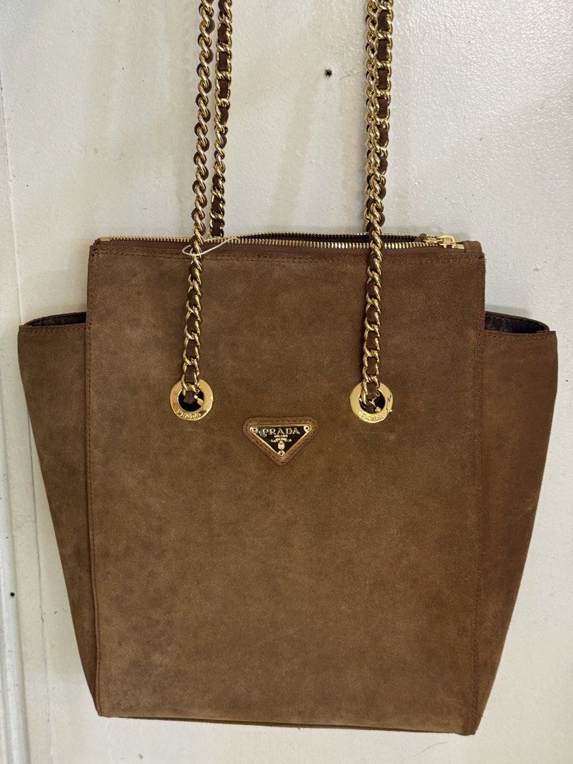 Prada Suede Chain Shoulder Bag (Category: Luxury Bags & Wallets) located in Marikina City. Submitted by _julianpaolo (Listing ID 1451814250, Image 1). Description: - Self-authenticated brown suede Prada shoulder bag from EU thrift shop - Elegant gold chain straps with suede detailing - Secure zipper closure at the top - Iconic Prada triangle logo prominently displayed - Versatile for everyday use or evening events - Offers a flattering shape and 