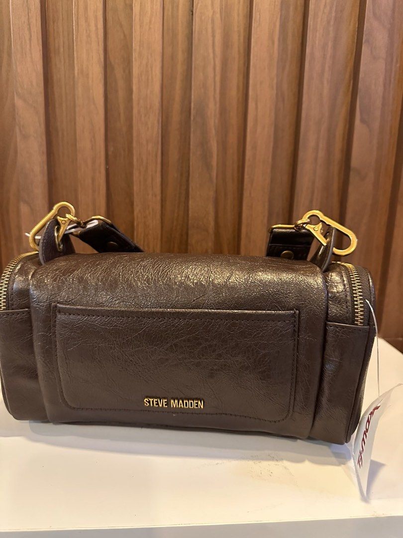 Steve Madden Brown Barrel Bag with Gold Hardware (Category: Luxury Bags & Wallets) located in Makati City. Submitted by sebastiene (Listing ID 1451785834, Image 1). Description: - Cool barrel-shaped bag from Steve Madden - Dark brown color with a textured finish - Stylish gold hardware details (zippers, chain strap accents) - Convenient front pocket - Detachable crossbody strap for versatile wear - Ideal for everyday use or a night out.