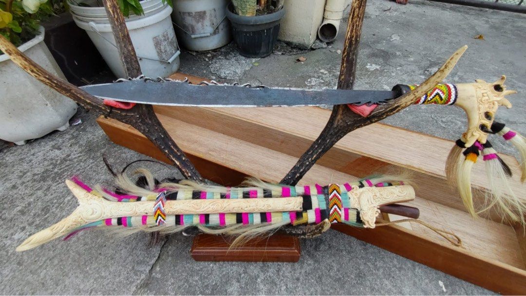 Antique Tribal Knife (Category: Vintage Collectibles) located in Cainta. Submitted by danica010314 (Listing ID 1452036915, Image 3). Description: This item is a traditional Dayak Mandau sword from Borneo, featuring a detailed carved hilt made of deer horn and a sheath adorned with colorful fabrics and goat hair.- Unique decorative knife set - Features carved bone handles - Colorful woven accents - Sharp blades with a rustic finish - Ideal for col