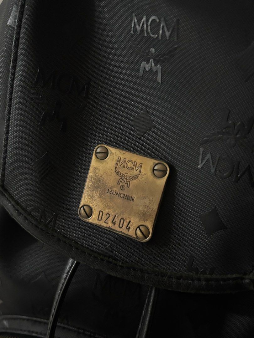 Authentic Vintage MCM Black Monogram Nylon Backpack with Gold Hardware Plaque (Category: Luxury Bags & Wallets) located in Masantol. Submitted by duhitsangelene (Listing ID 1452036368, Image 3). Description: Product Details: Brand: MCM (Modern Creation München) Color: Black with subtle jacquard monogram print Material: Durable nylon / canvas body with leather trim Closure: Magnetic flap over drawstring closure Pockets: One front zippered compartm