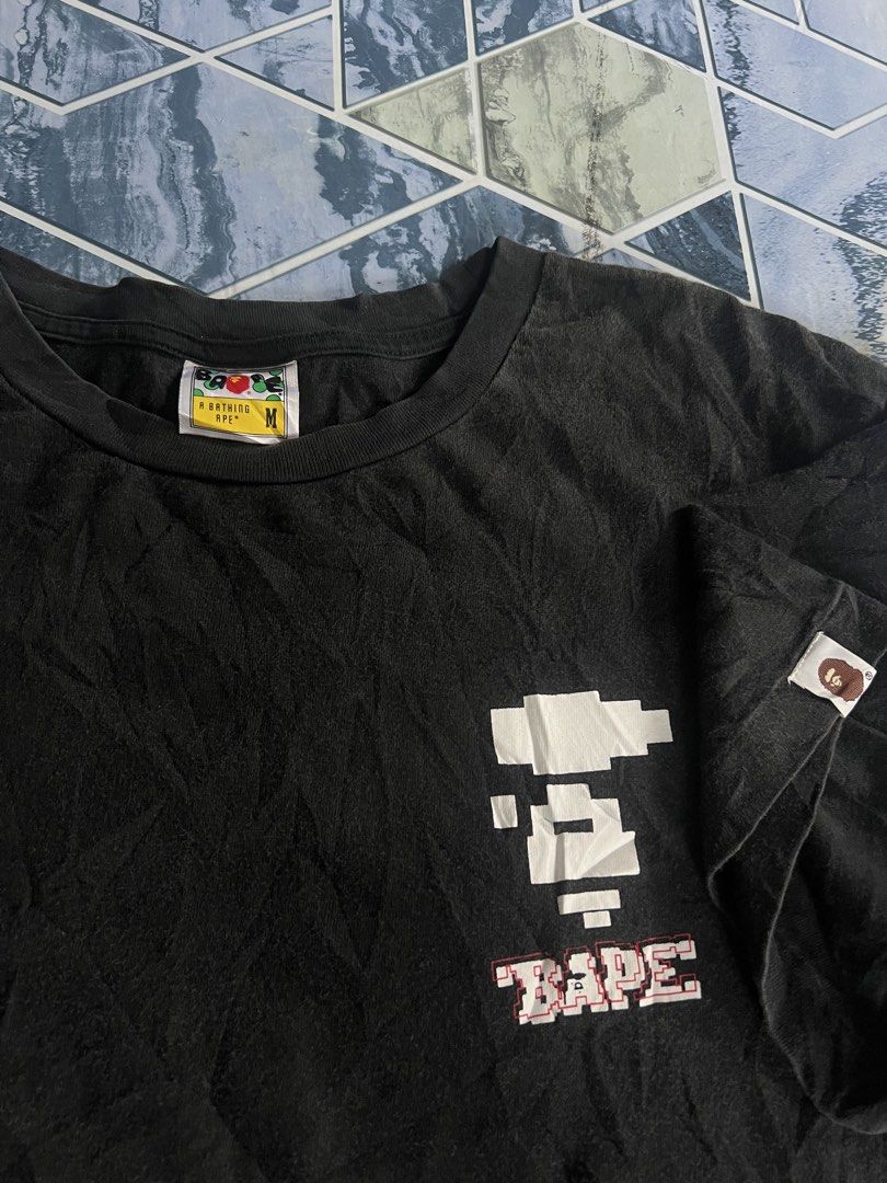 BAPE Pixel Ape & "BAPE" Logo Black T-Shirt (Category: Tshirts & Polo Shirts ) located in Manila. Submitted by thrifttolive (Listing ID 1451962282, Image 3). Description: - Authentic BAPE T-shirt - Size: Medium (M) - Front: Pixelated Ape Head graphic with 'BAPE' text - Back: 'BAPE' text in camouflage pattern - Sleeve: Small BAPE tag detail -Dimes:21x27 -Good condition -No issues .