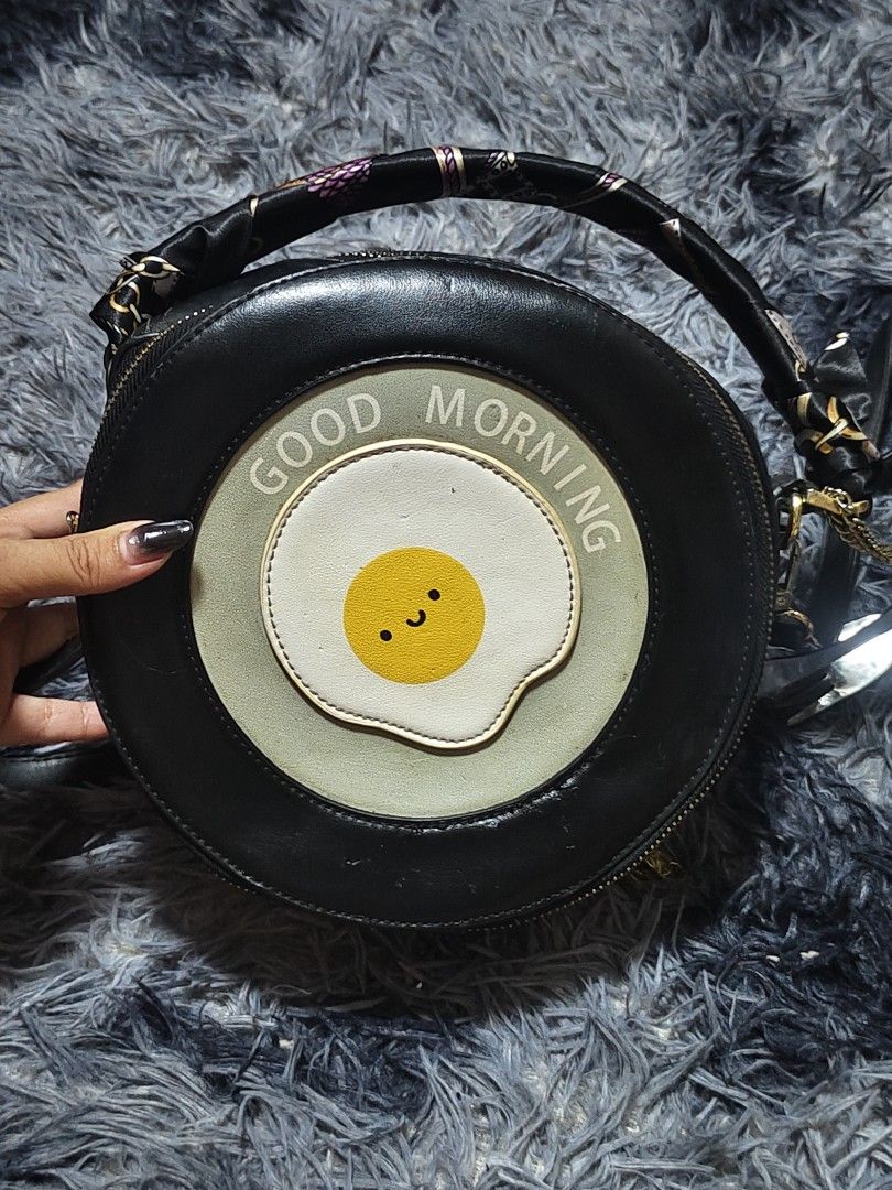 Cute Fried Egg Round Japanese Bag with Scarf Handle (Category: Cross-body Bags) located in Manila. Submitted by querobin11 (Listing ID 1452039972, Image 1). Description: - Adorable round bag with a fun fried egg design. - Features 'Good Morning' text for a cheerful vibe. - Stylish scarf-wrapped handle. - Includes a long strap for versatile carrying options. - Accented with elegant gold hardware. - Adds a playful and unique touch to any outfit. RF
