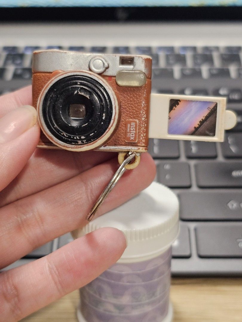 Fujifilm Instax Mini 90 Keychain (Category: Cameras) located in Paranaque City. Submitted by viviperera (Listing ID 1452098932, Image 1). Description: - Adorable keychain shaped like a Fujifilm Instax Mini 90 camera. - Features a tiny slot to display a mini photo. - Stylish brown and silver camera body. - Includes a sturdy keyring for easy attachment. - Ideal gift for photography enthusiasts or a fun personal accessory..