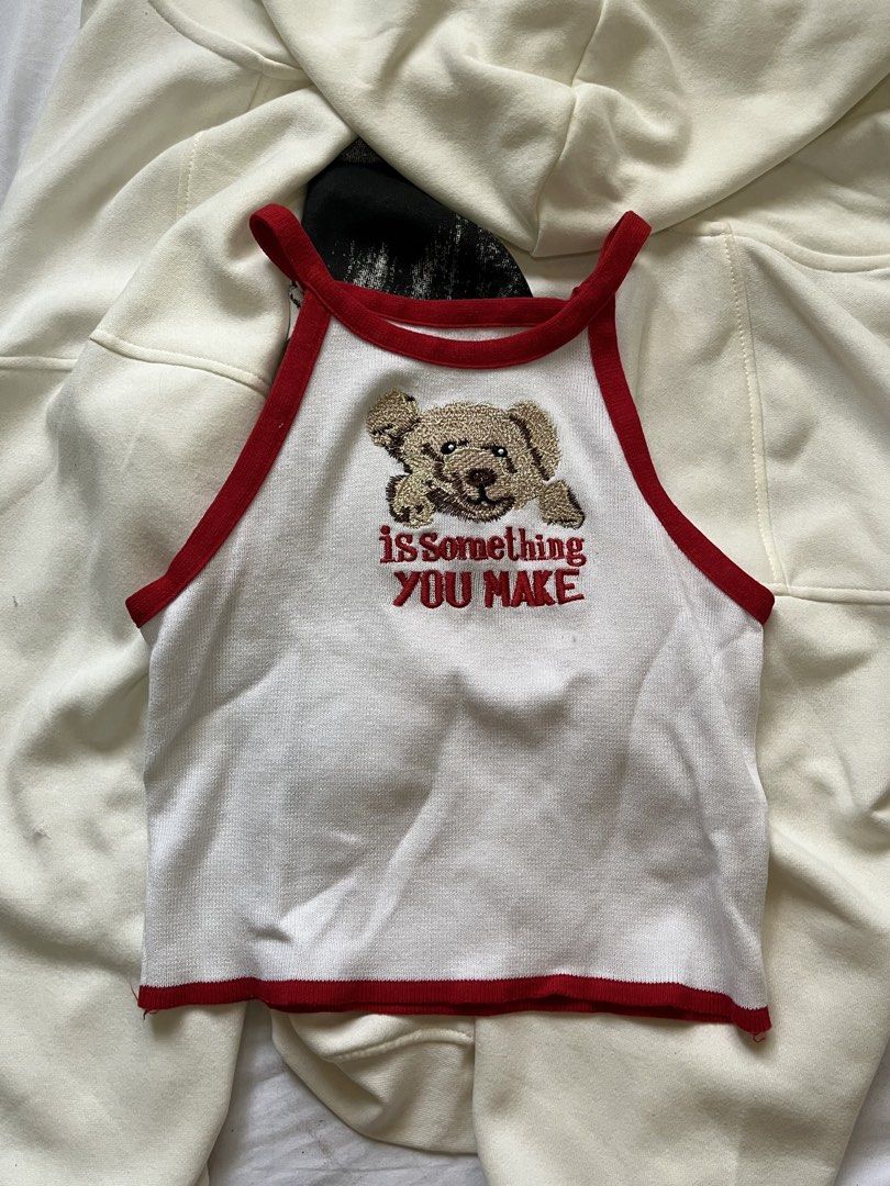 White Teddy Bear Embroidered Crop Top with Red Trim (Category: Others Tops) located in Paranaque City. Submitted by bymuse.co (Listing ID 1452008677, Image 1). Description: - Adorable white crop top - Features a cute teddy bear embroidery with 'is something YOU MAKE' text - Stylish red trim along the neckline and hem - Sleeveless halter design - Perfect for casual outfits or layering - Fits like a size Small.