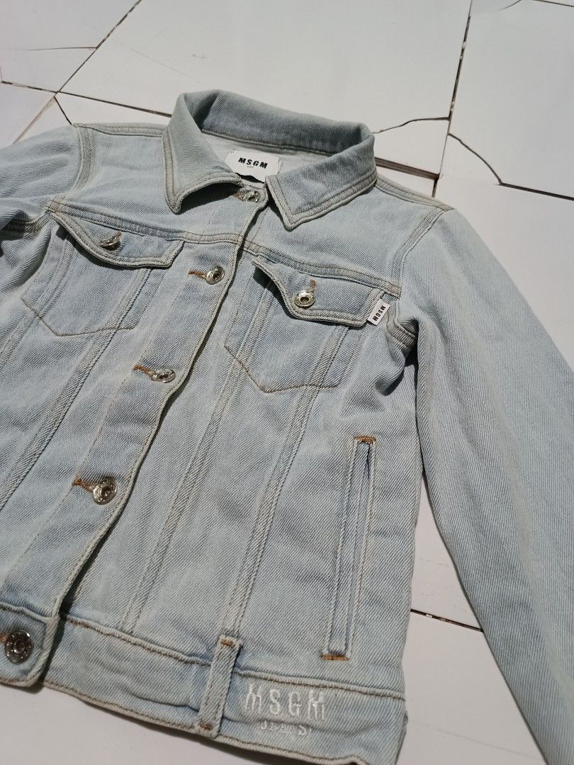 MSG M Kids Light Wash Denim Jacket (Category: Babies & Kids Fashion) located in Barotac Nuevo. Submitted by gray101 (Listing ID 1452445923, Image 2). Description: - MSGM Kids light wash denim jacket - Features iconic MSGM logo printed on the back - Classic button-up front with chest pockets - Made from soft cotton with added stretch for comfort - Size: Tag says Tg. 10 Anni (approximately 10 years old) - Perfect for stylish everyday wear.