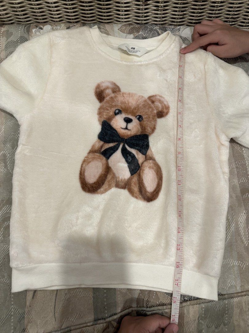 H&M Teddy Bear Fleece Sweatshirt (Category: Babies & Kids Fashion) located in Manila. Submitted by bubuamponin (Listing ID 1447299195, Image 3). Description: - Cream colored fleece sweatshirt from H&M - Features a cute teddy bear graphic with a black bow - Long sleeves and crew neck - Soft and cozy material, great for casual wear - Measurements: Length 18", Chest 14", Sleeve 15" - Note: Slight yellow stain near the collar.