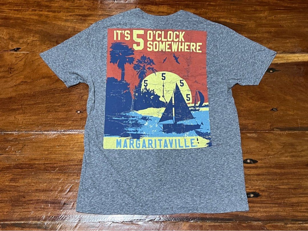 Margaritaville Graphic T-Shirt (Category: Tshirts & Polo Shirts ) located in Leyte. Submitted by jcatle (Listing ID 1447453984, Image 2). Description: - Grey heather t-shirt - Fits M-L - Fun 'It's 5 O'Clock Somewhere' graphic on the back - Graphic includes sailboat and palm trees - Small Margaritaville logo on the front chest - Ideal for casual wear or a beach vibe.
