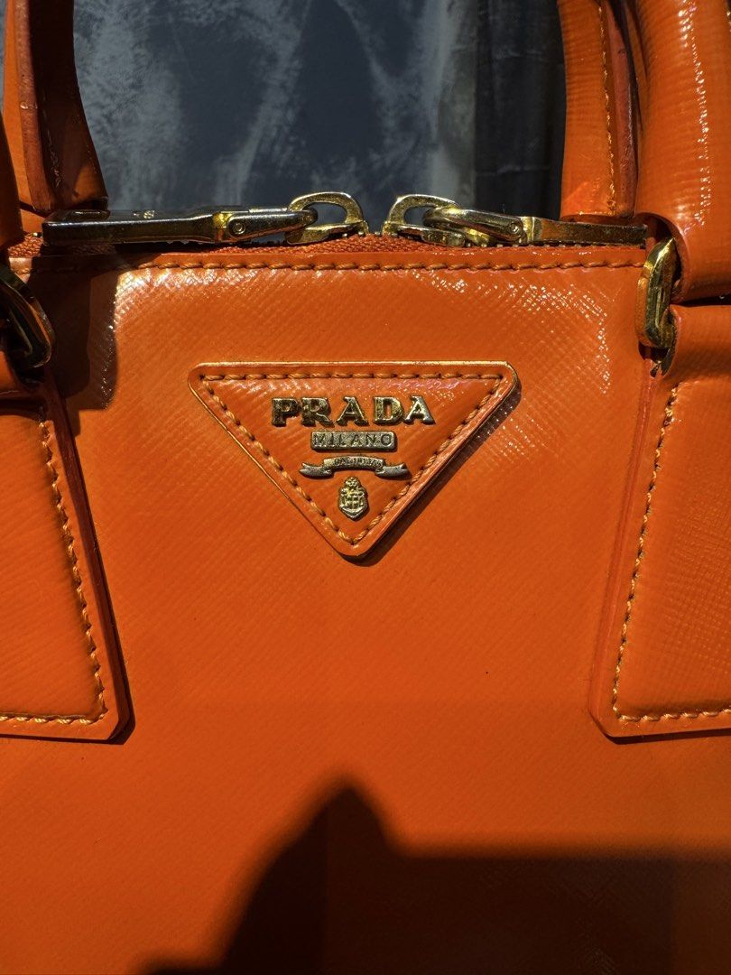 Prada Orange Patent Leather Top Handle Bag with Strap (Category: Luxury Bags & Wallets) located in Santiago. Submitted by twicebutnice03 (Listing ID 1447397683, Image 3). Description: - Authentic Orange Prada Bag - Glossy Patent Leather Finish - Includes Detachable Shoulder Strap - Elegant Gold Hardware Details - Versatile: Ideal for everyday or evening wear - Spacious Interior for Essentials - A Timeless Addition to Your Collection.