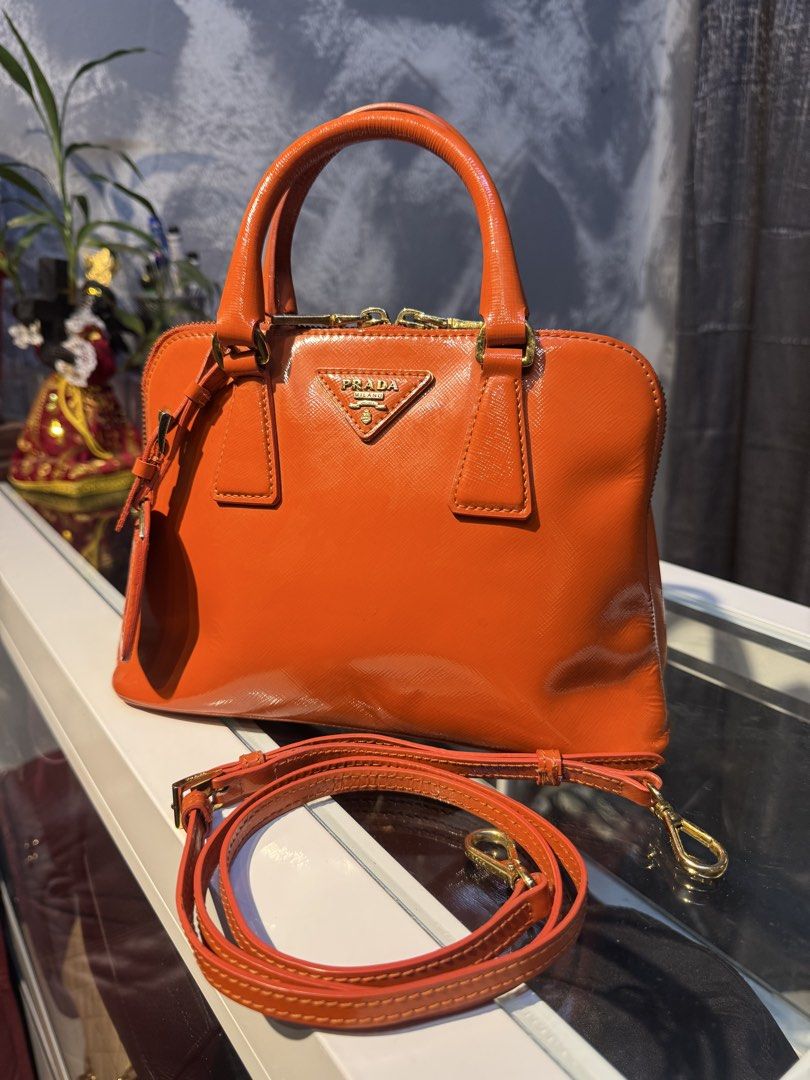 Prada Orange Patent Leather Top Handle Bag with Strap (Category: Luxury Bags & Wallets) located in Santiago. Submitted by twicebutnice03 (Listing ID 1447397683, Image 2). Description: - Authentic Orange Prada Bag - Glossy Patent Leather Finish - Includes Detachable Shoulder Strap - Elegant Gold Hardware Details - Versatile: Ideal for everyday or evening wear - Spacious Interior for Essentials - A Timeless Addition to Your Collection.