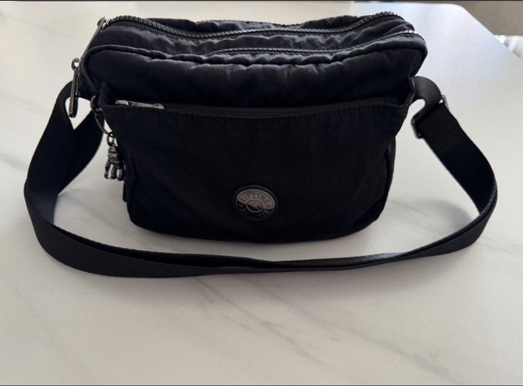 Authentic Kipling (Category: Cross-body Bags) located in Singapore. Submitted by blessingbabe (Listing ID 1452709672, Image 2). Description: - Authentic Kipling ABANU M Endless Black Crossbody Bag - Durable and lightweight nylon material - Classic and versatile black color - Adjustable crossbody strap for comfortable wear - Features the iconic Kipling monkey charm - Multiple zippered compartments for organization - Ideal for everyday use, travel,