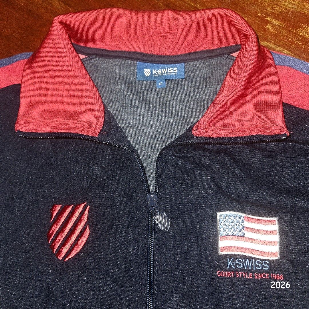 K-Swiss Track Jacket Navy Red Blue Size M (Category: Coats, Jackets and Outerwear) located in Bislig. Submitted by edisontv (Listing ID 1452731864, Image 2). Description: - Classic K-Swiss track jacket - Color: Navy blue with red and blue sleeve/collar stripes - Features K-Swiss logo with "Court Style Since 1966" print - Includes an American flag patch - Material: 86% polyester, 14% cotton - Tagged Size: M - Ideal for casual wear or sports activi