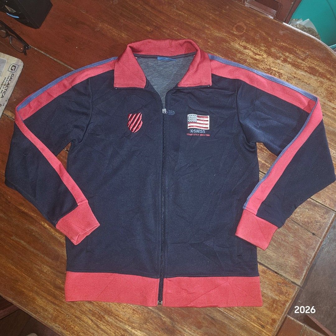 K-Swiss Track Jacket Navy Red Blue Size M (Category: Coats, Jackets and Outerwear) located in Bislig. Submitted by edisontv (Listing ID 1452731864, Image 1). Description: - Classic K-Swiss track jacket - Color: Navy blue with red and blue sleeve/collar stripes - Features K-Swiss logo with "Court Style Since 1966" print - Includes an American flag patch - Material: 86% polyester, 14% cotton - Tagged Size: M - Ideal for casual wear or sports activi