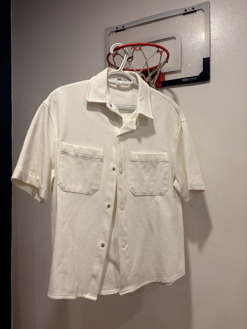 ZARA White Short Sleeve Button Up Shirt (Category: Tshirts & Polo Shirts ) located in Quezon City. Submitted by rafaisip (Listing ID 1452922656, Image 1). Description: - ZARA white short sleeve button up shirt - Features two chest pockets with button closures - Simple and clean design - Versatile for casual wear or layering.
